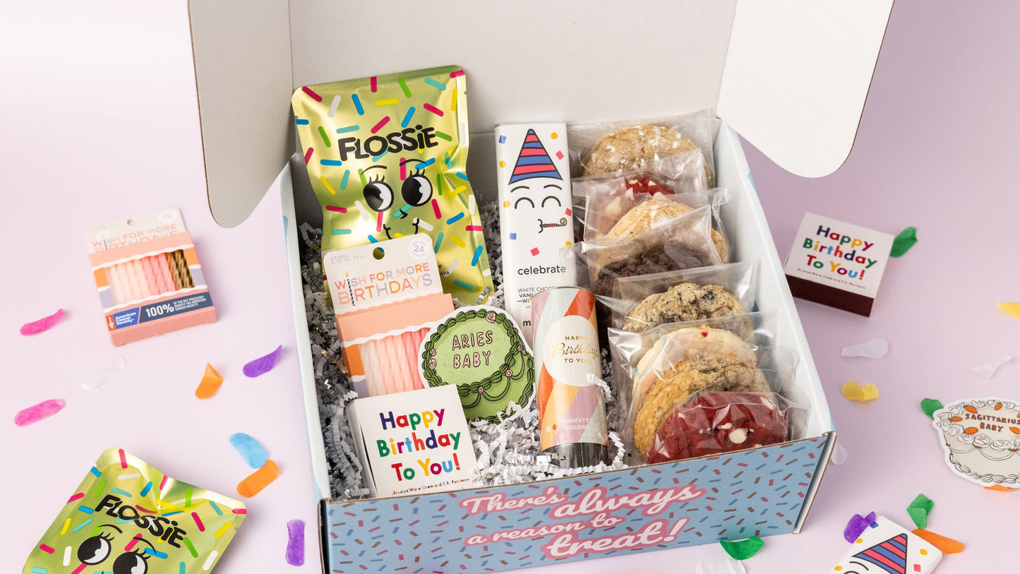 Birthday-themed gift box featuring individually wrapped cookies, a "Celebrate" white chocolate birthday cake bar, Flossie birthday cake candy, pink birthday candles, a confetti popper, and a "Happy Birthday to You" matchbox. The box reads, "There's always a reason to treat!" with colorful confetti scattered on a light pink background.