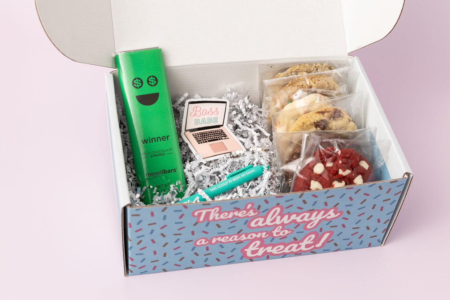 Boss-themed gift box featuring individually wrapped cookies, a "Winner" milk chocolate s'mores bar, a "Boss Babe" laptop sticker, and a teal pen that reads "This Could've Been an Email." The box reads, "There's always a reason to treat!" with shredded paper filler and a light pink background.